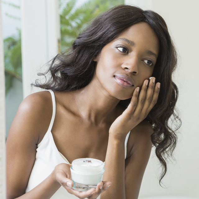 Femme se mettant de la crème sur le visage dans une salle de bain (Istock)